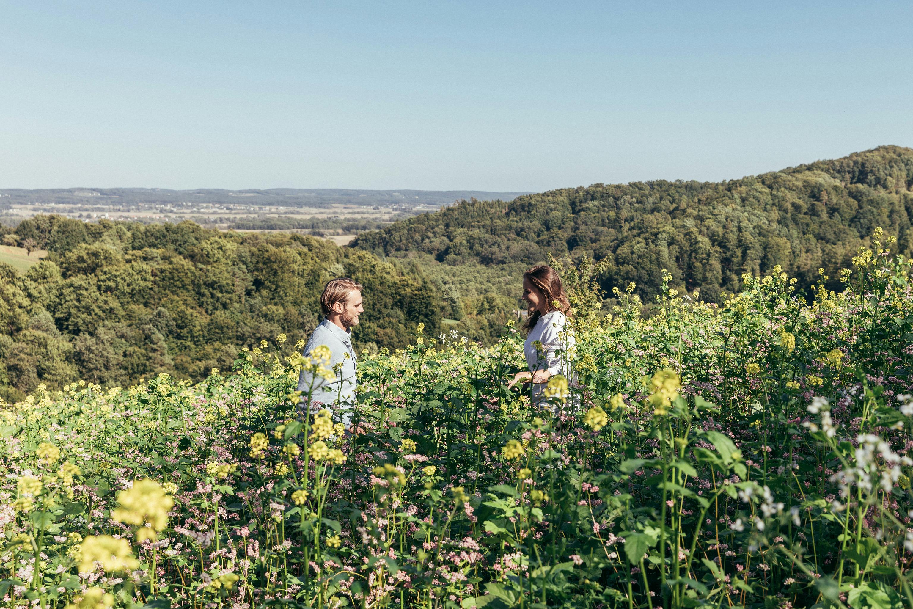 Pärchen steht in der Wiese und im Hintergrund ist die Landschaft rund um Bad Loipersdorf zu sehen.