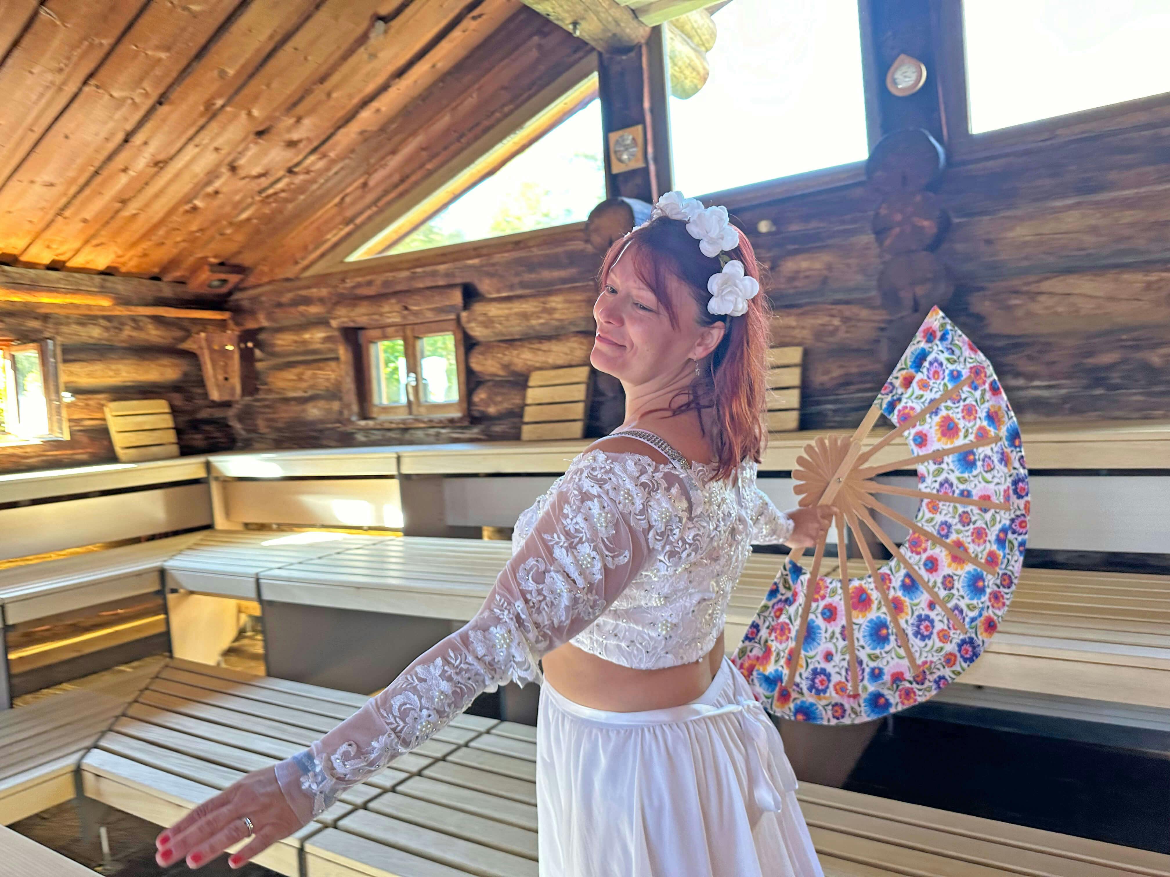 Verkleidete Aufgussmeisterin in der Panoramasauna im Schaffelbad mit weißem Kleid und bunten Fächer in der Hand.