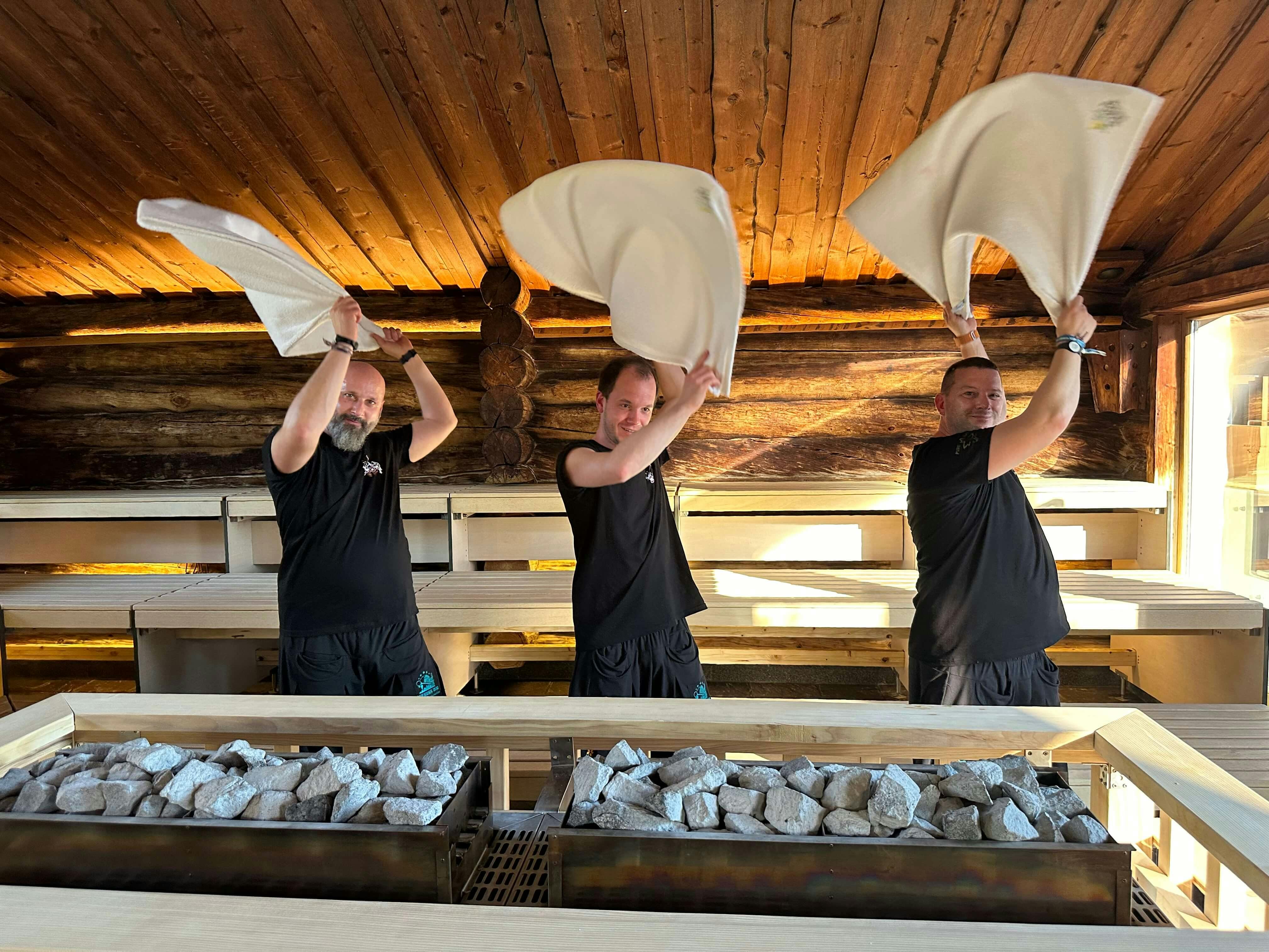 Drei Aufgussmeister in der Panoramasauna im Schaffelbad mit großen Saunatüchern in der Luft.