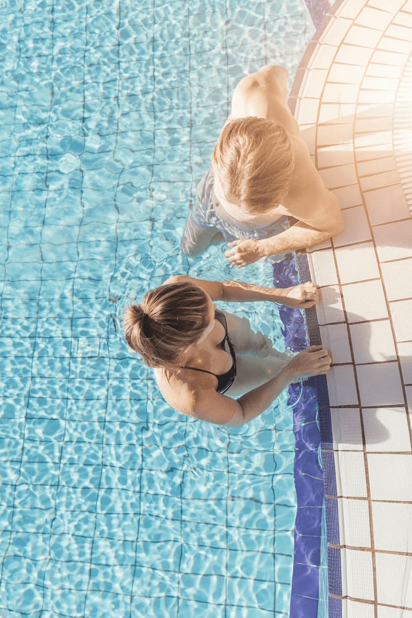 Pärchen im Wasser stehend am Beckenrand, eine mit blondem, die andere mit dunklem Haar
