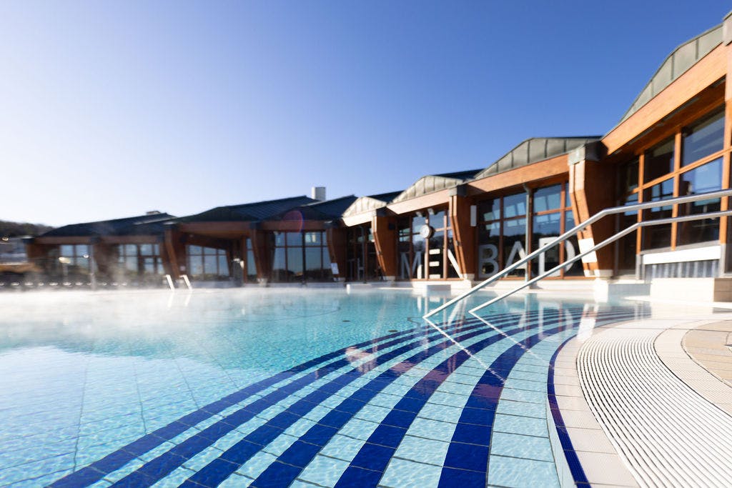 Blick auf das Thermalwasser im Thermalbecken-Außen. Im Hintergrund ist die Architektur der Therme gut zu erkennen.
