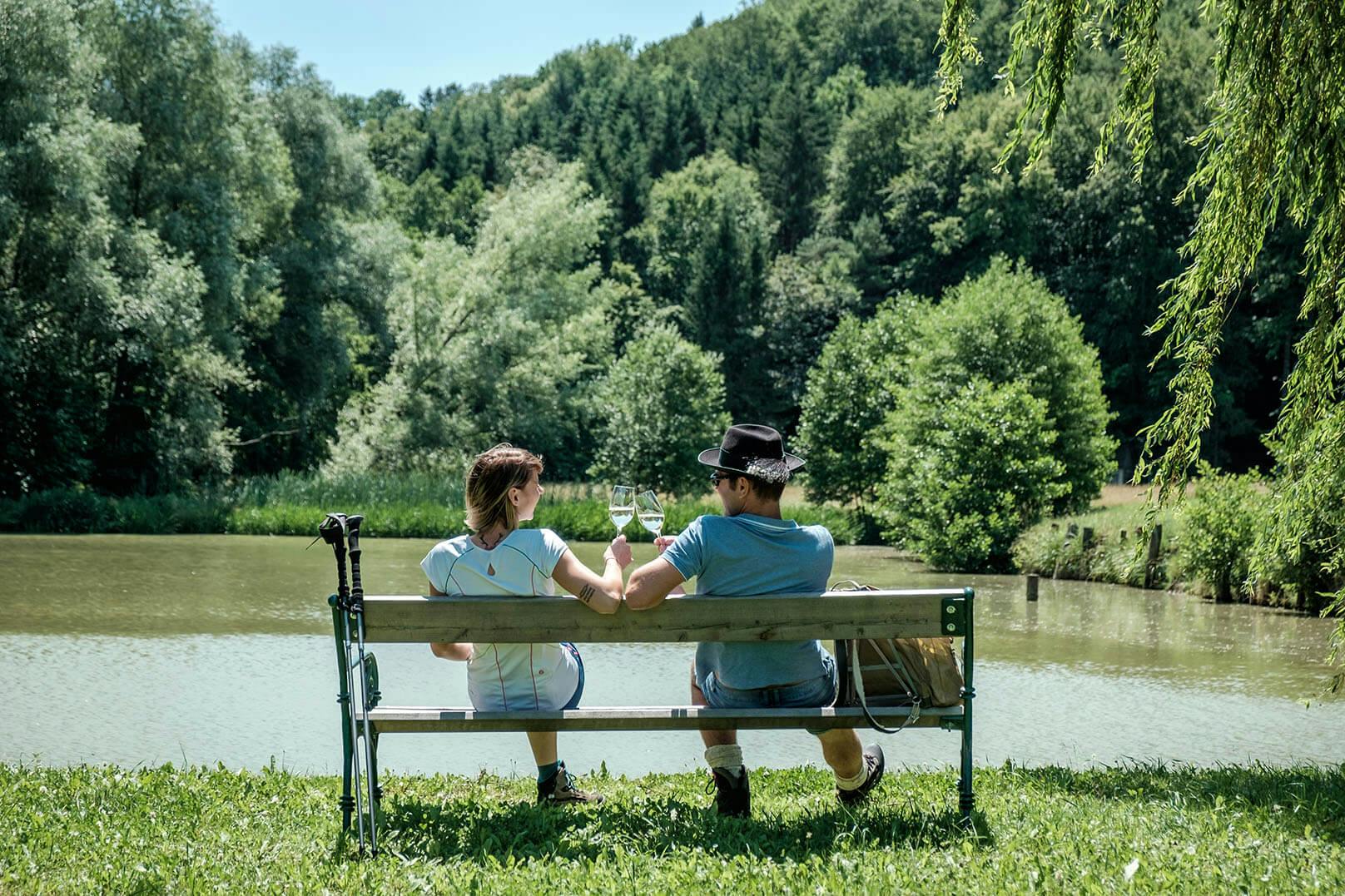 A couple drinking wine by the pond in the sunshine.