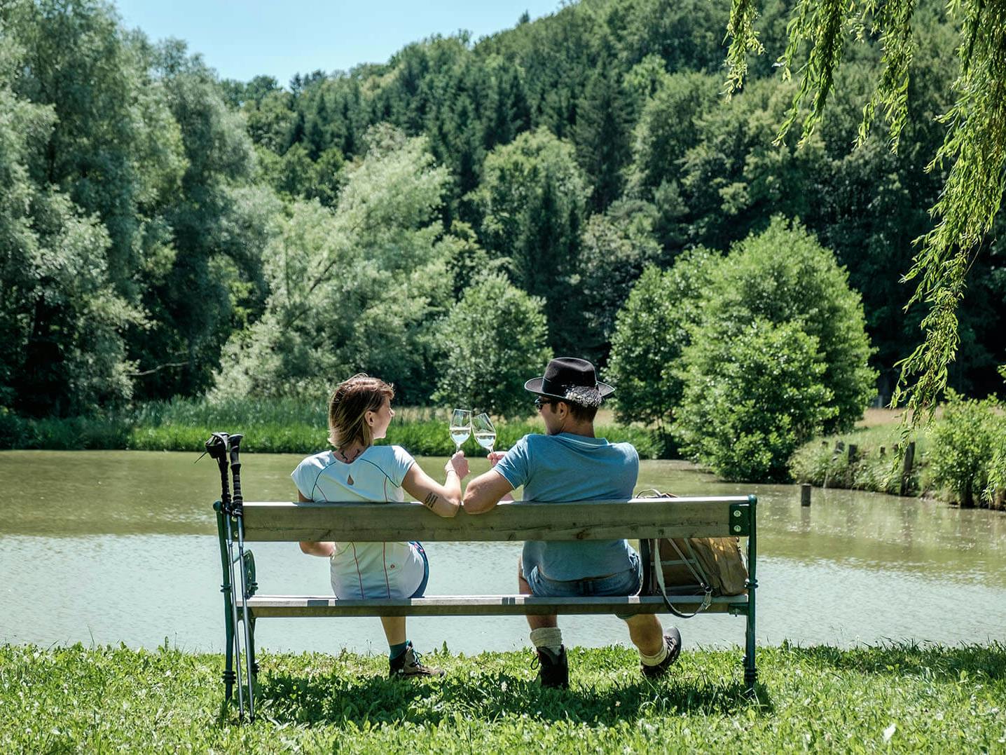 A couple drinking wine by the pond in the sunshine.