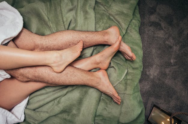 Die Füße eines Paares beim Kuscheln auf einer Decke.