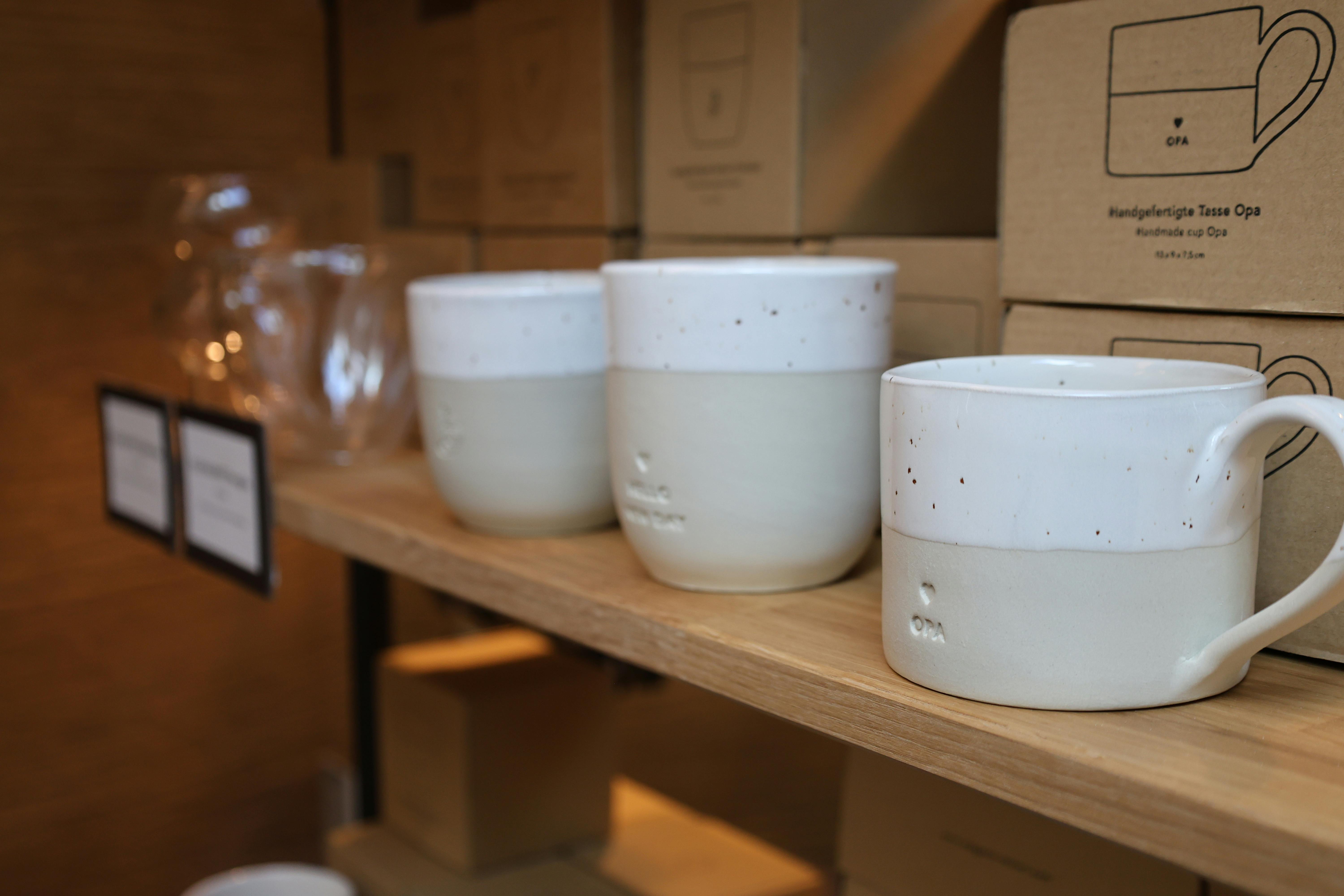 Drei handgefertigte Tassen in Weiß mit grauem Unterteil und feinen schwarzen Sprenkeln stehen auf einem Holzregal.