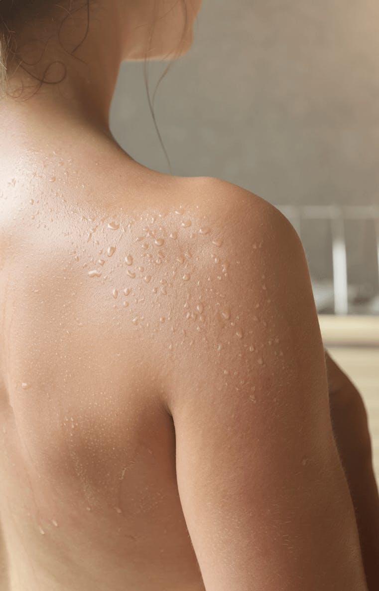 Nackter Rücken und Schulter einer Person mit Wassertropfen auf der Haut vor unscharfem Hintergrund