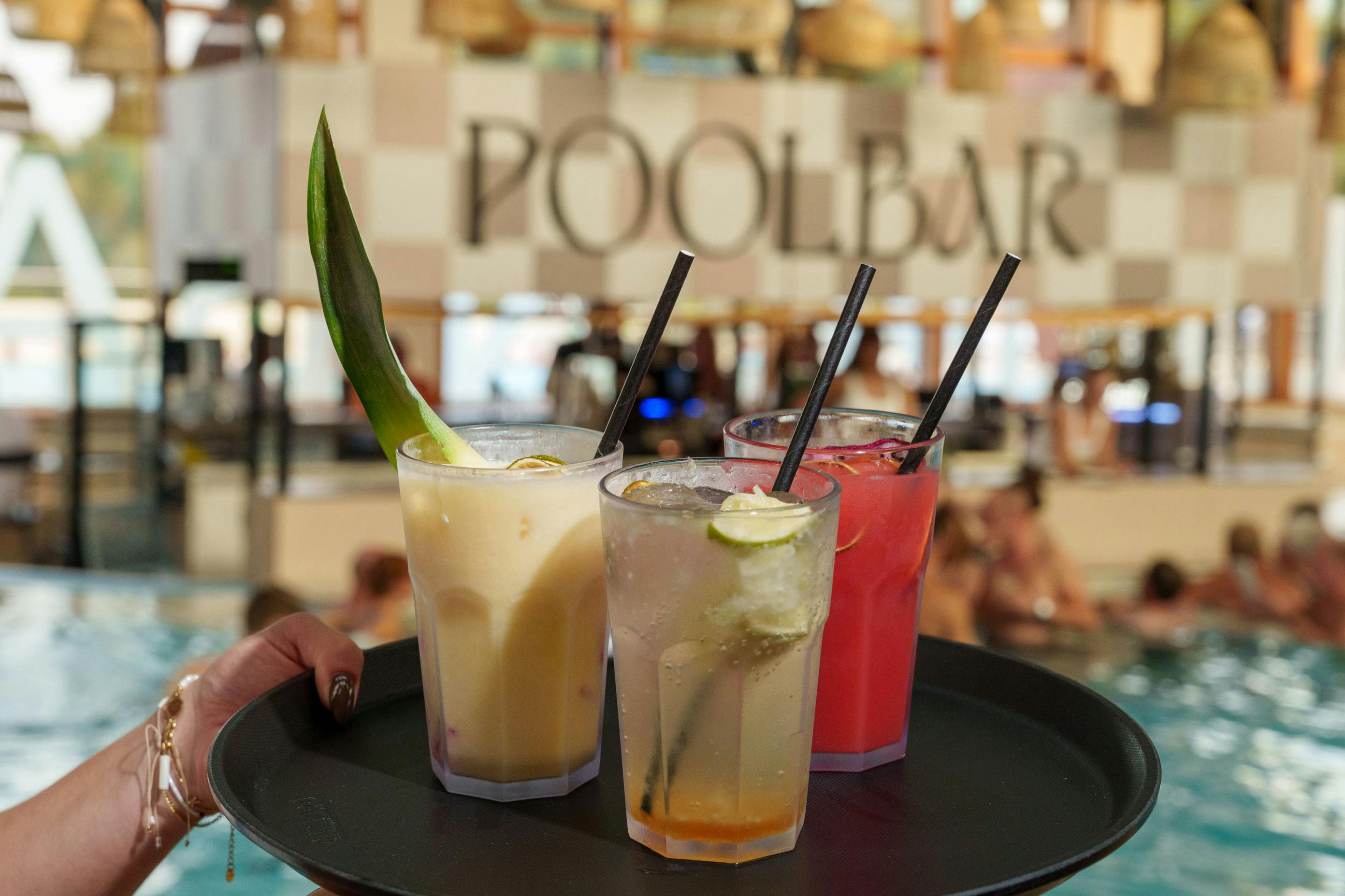 Leckere Cocktails auf einem Tablett und im Hintergrund sieht man die Poolbar im Thermenresort Loipersdorf.