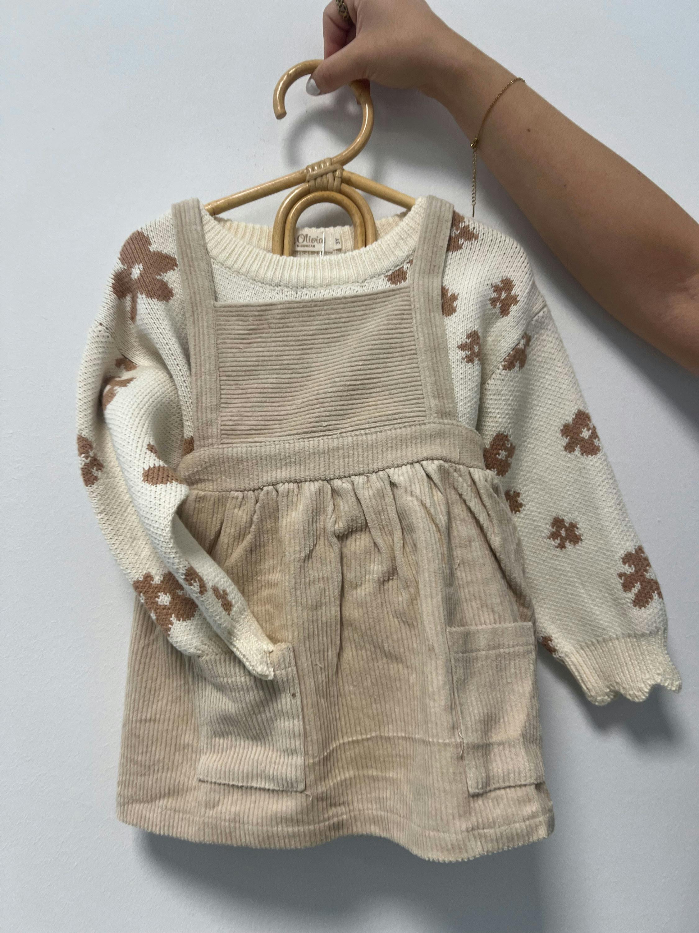 Beige Cordkleid mit Taschen über einem cremefarbenen Pullover mit braunen Blumenmuster, an einem Holzkleiderbügel gehalten.