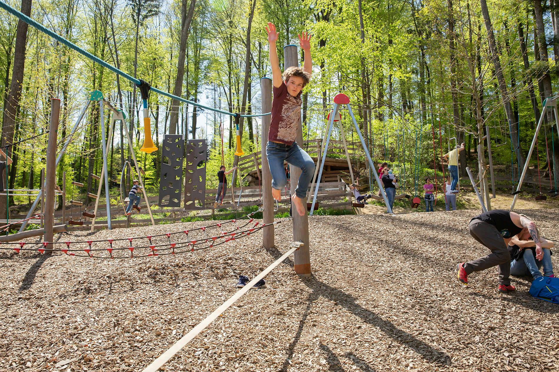 Ein Junge klettert im Waldspielplatz über ein Netz.